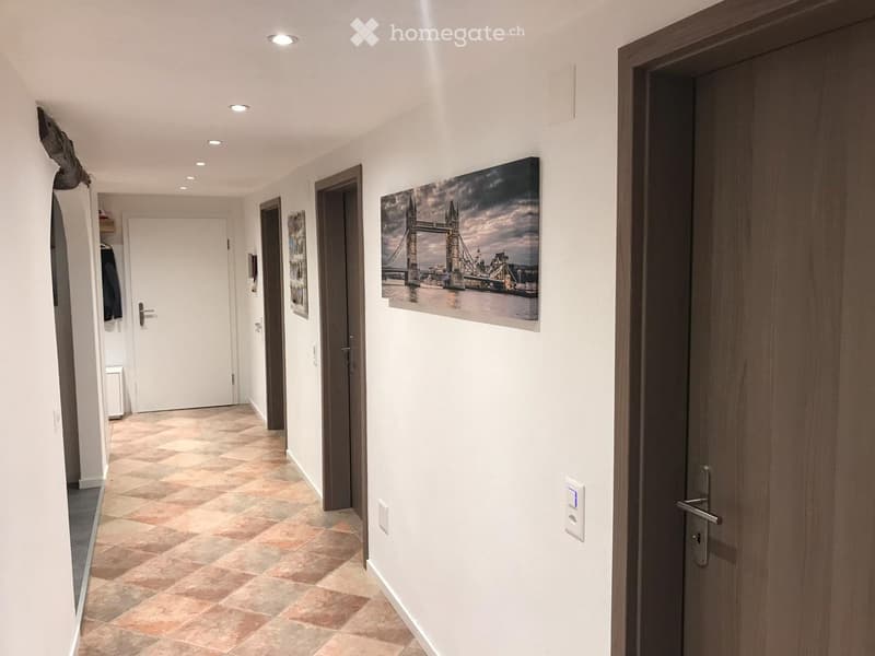 Clean hallway with tiled floor, recessed lighting, several doors, and artwork on the walls.