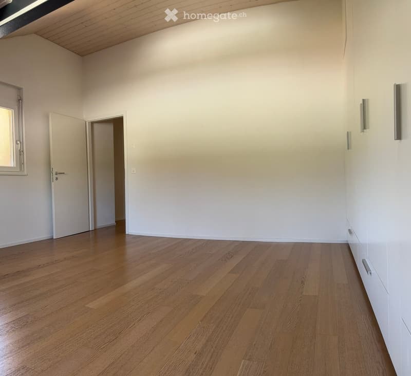 Empty room with wooden flooring, white walls, and two doors, one leading to another room and the other to a window.