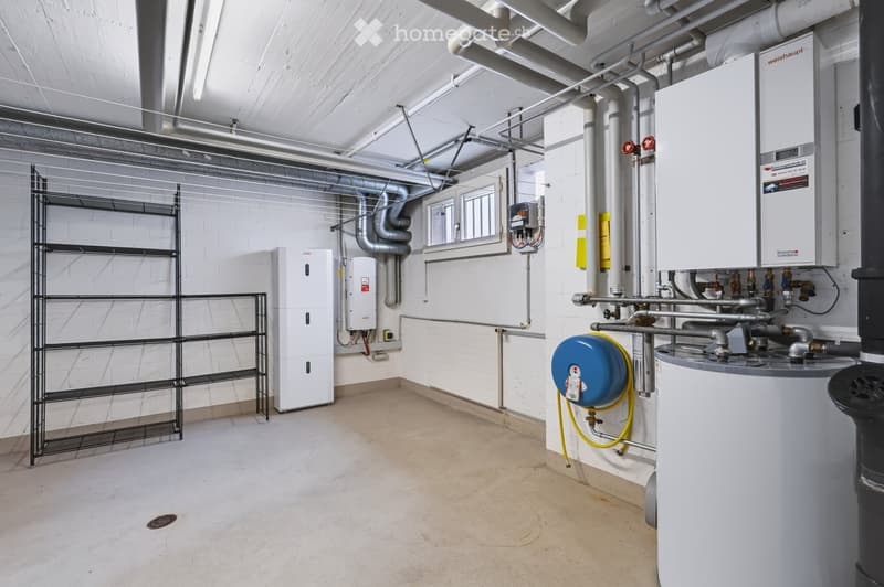 The image shows an unfurnished utility room with white brick walls, exposed pipes, and various heating and water systems, including a water heater, boiler, and shelving unit.