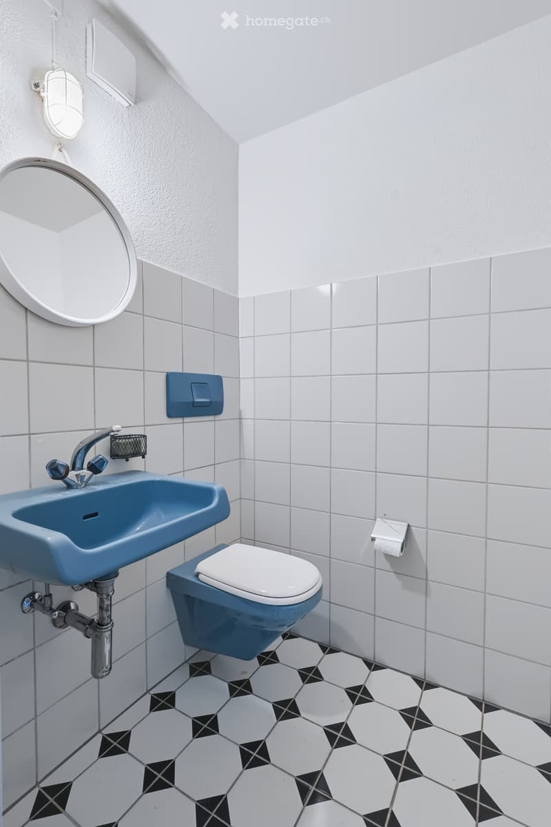 Modern bathroom with white and blue tiles, a blue sink, a white toilet, and a round mirror on the wall.