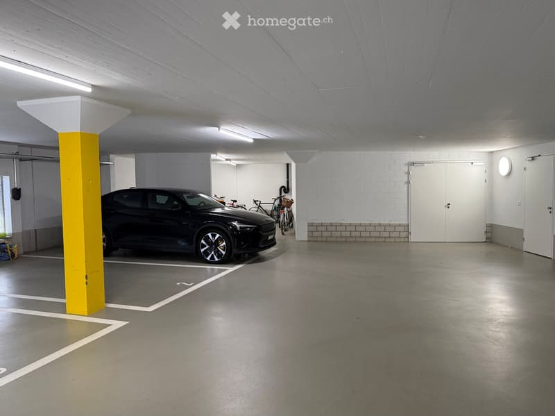 Underground parking area with a parked car, bicycles, and a yellow support column.