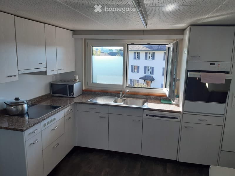 Modern kitchen with white cabinets, granite countertops, stainless steel appliances, and a large window overlooking a residential area.