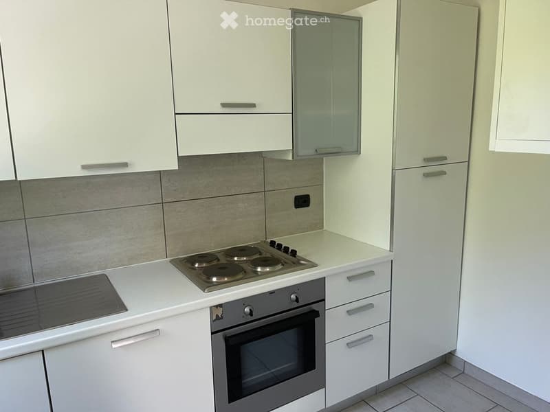 Modern kitchen with white cabinets, a built-in oven, and a four-burner stove. The countertops are white, and the backsplash features a gray tile design.