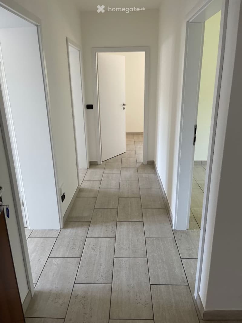 Empty hallway with tiled floor, white walls, and multiple doors.