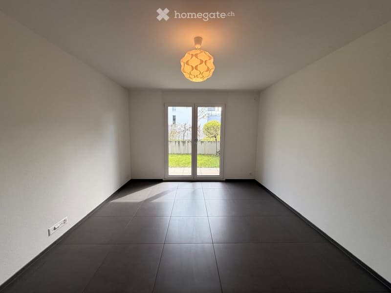 Empty room with dark tiled floor, white walls, and a large sliding glass door leading to a garden area.