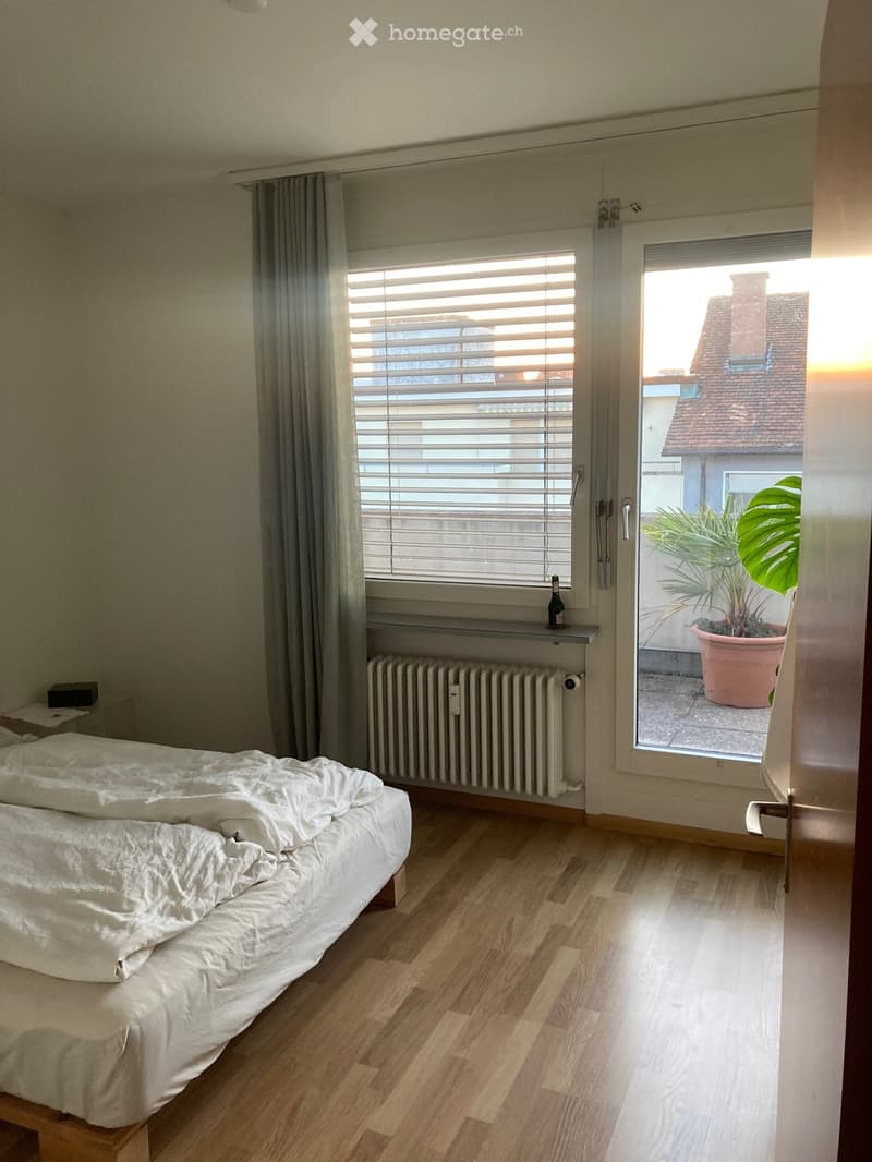 Bedroom with a double bed, wooden flooring, radiator, window with blinds, and a bottle on the windowsill.