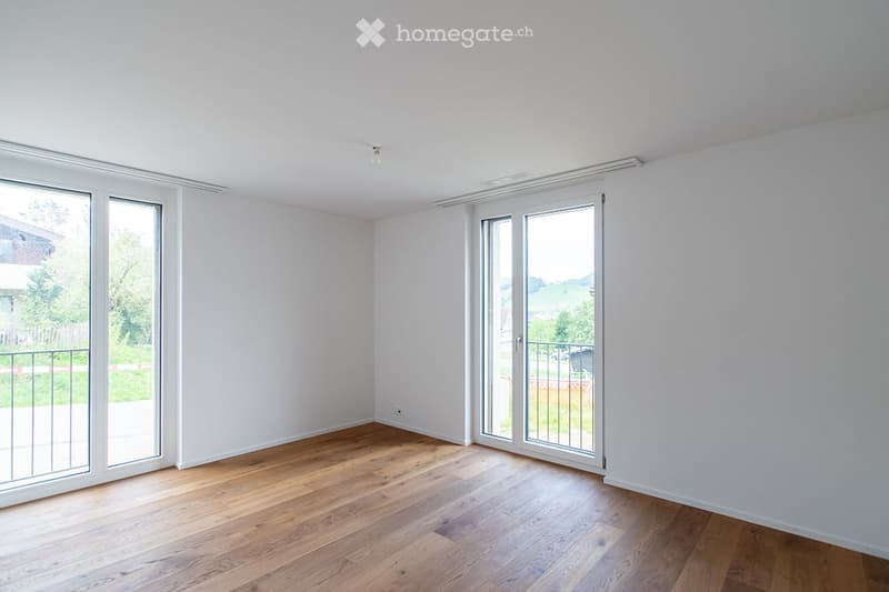 Empty room with wooden flooring, white walls, and large glass sliding doors leading to a balcony.