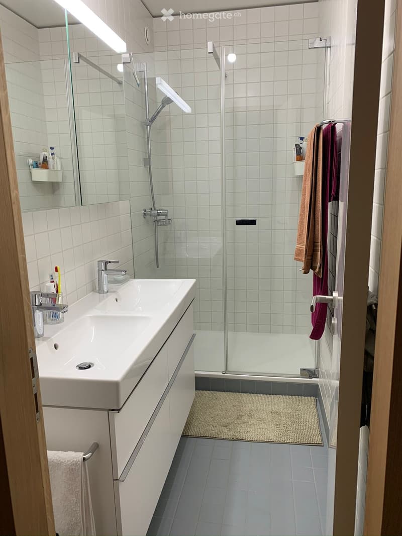 Modern bathroom with white tiled walls, a large sink with a modern faucet, a glass-enclosed shower, and neatly arranged towels and toiletries.
