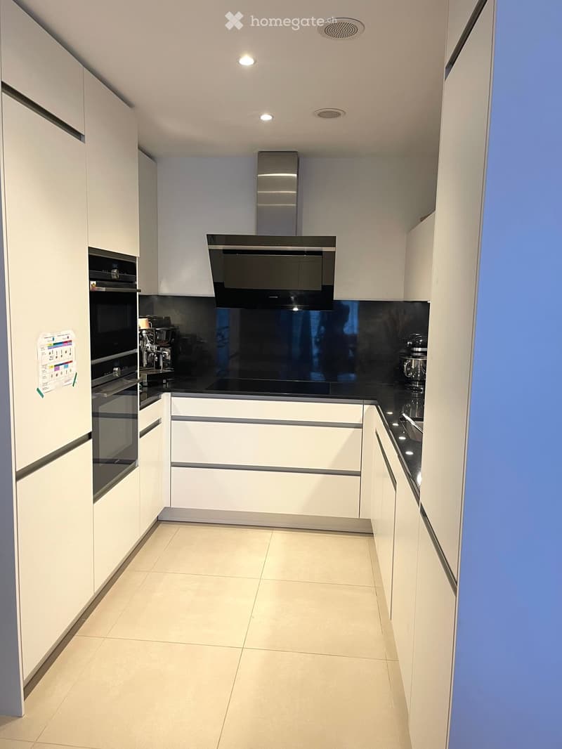 Modern kitchen with white cabinets, black countertops, and stainless steel appliances including an oven, coffee machine, and range hood.