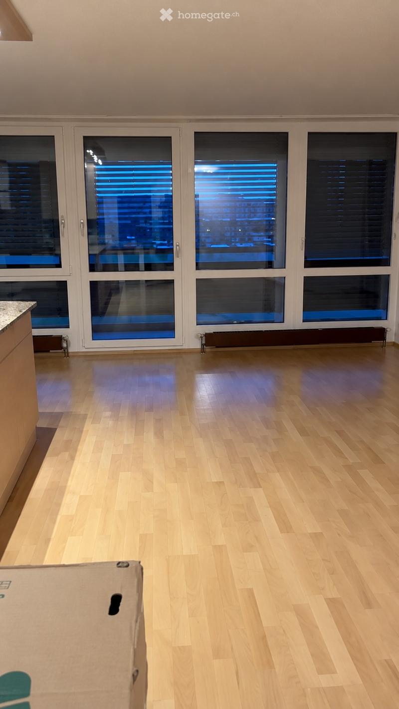 Empty room with wooden flooring, large windows with blinds, and a radiator under the windows.