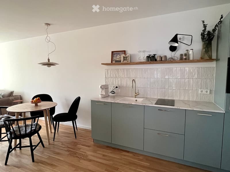 Modern kitchen with grey cabinets, marble countertop, sink, coffee machine, and a small dining area with a round table and chairs.