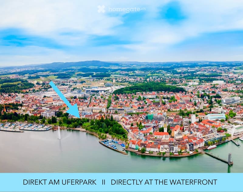 Aerial view of a town with a waterfront, featuring numerous buildings, a marina, and surrounding greenery.