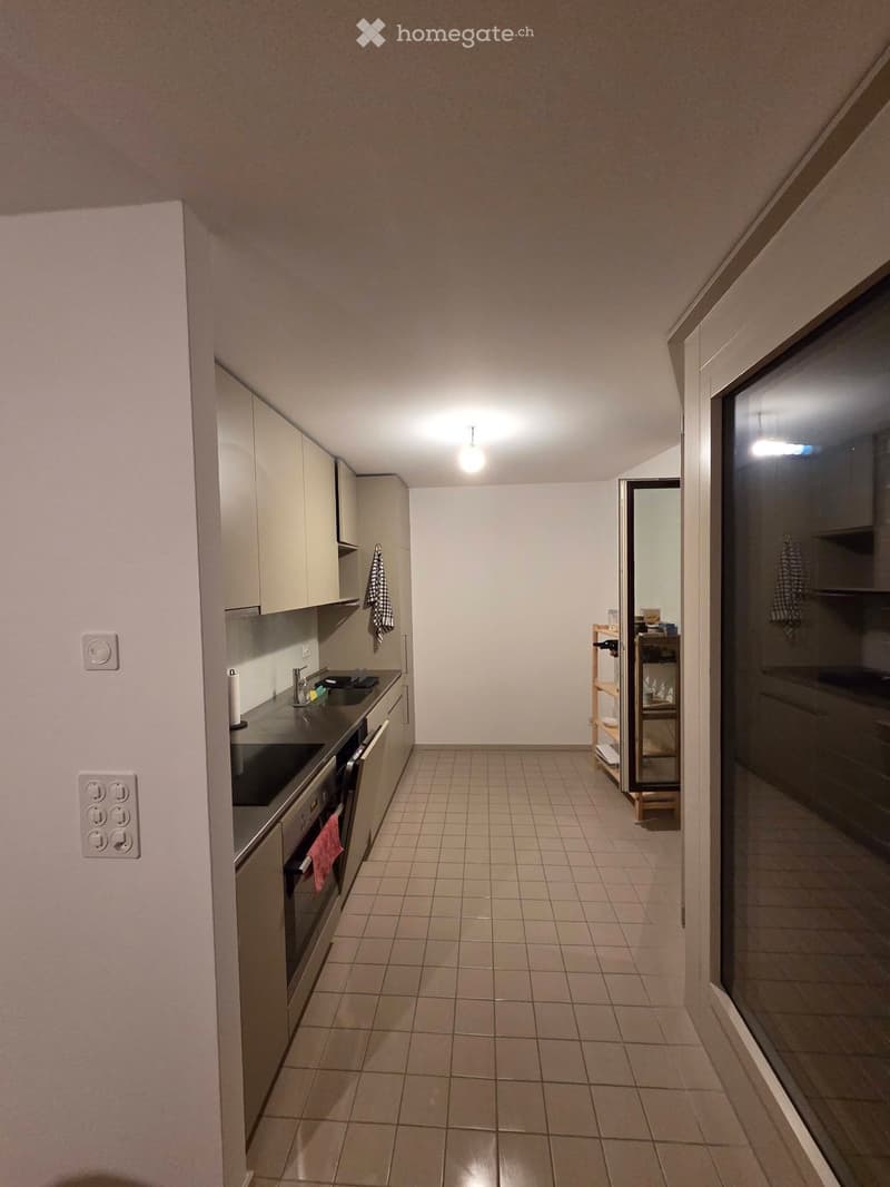 Modern kitchen with tiled floor, white cabinets, stainless steel sink, oven, and a small wooden shelf near the entrance.