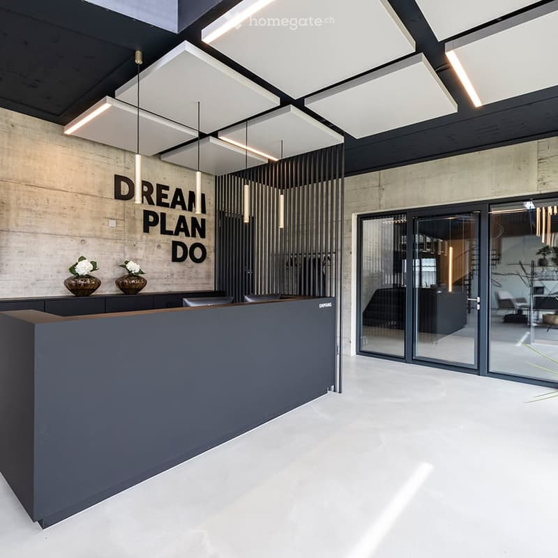 Modern reception area with a sleek black reception desk, two vases with white flowers, and a glass door leading to another room.