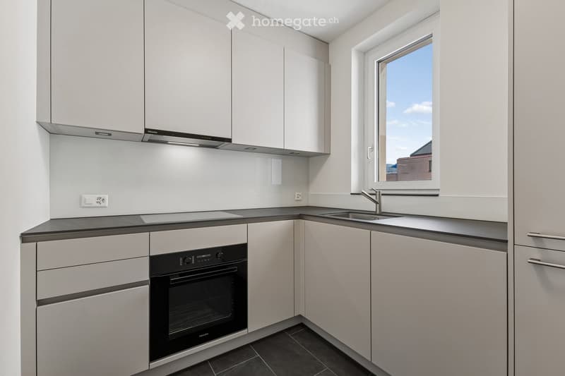 Modern kitchen with white cabinets, black countertop, built-in oven, and a window overlooking the outside.