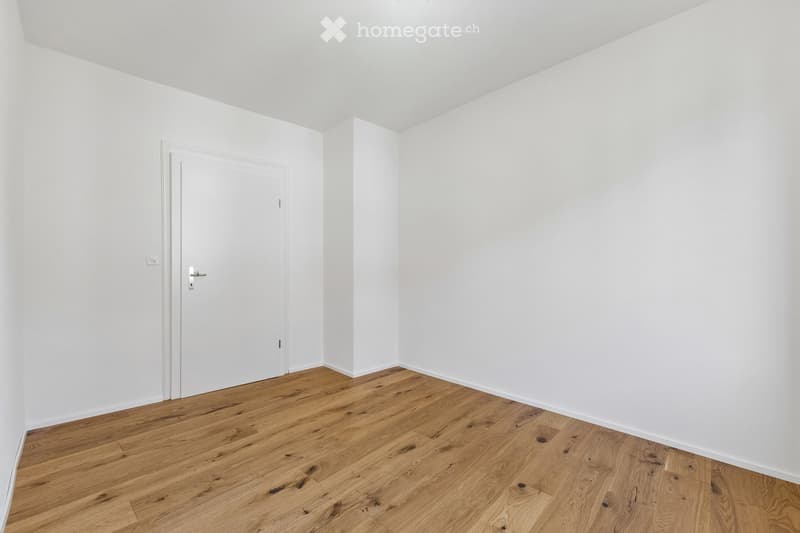 Empty room with white walls and wooden flooring, featuring a single white door.
