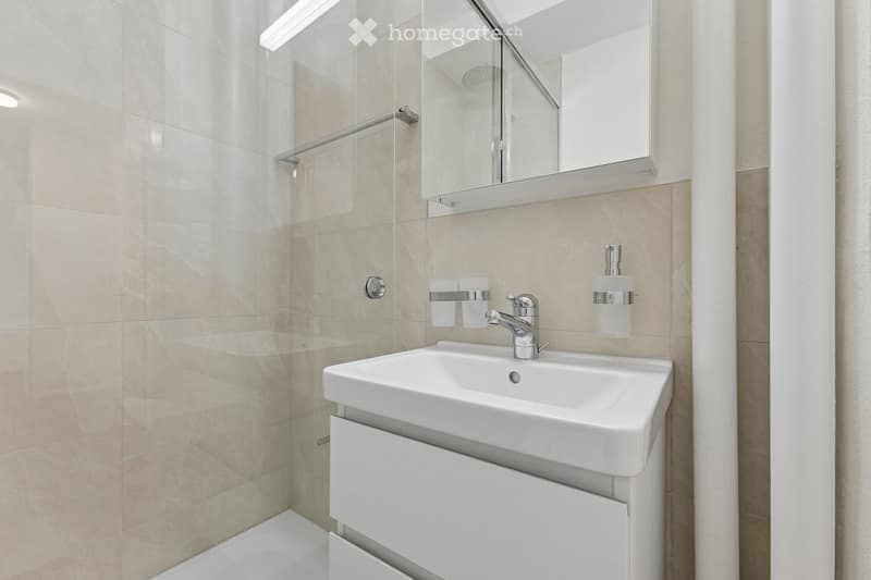 Modern bathroom with a white sink, chrome faucet, mirrored cabinet, and two cups on the counter.