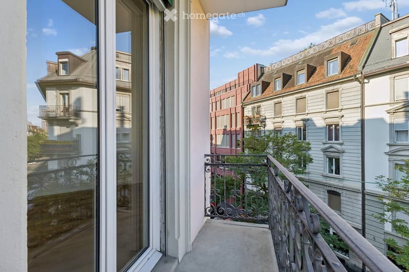 Balcony with metal railing overlooking a cityscape of historic buildings with varied architectural styles and rooftops.