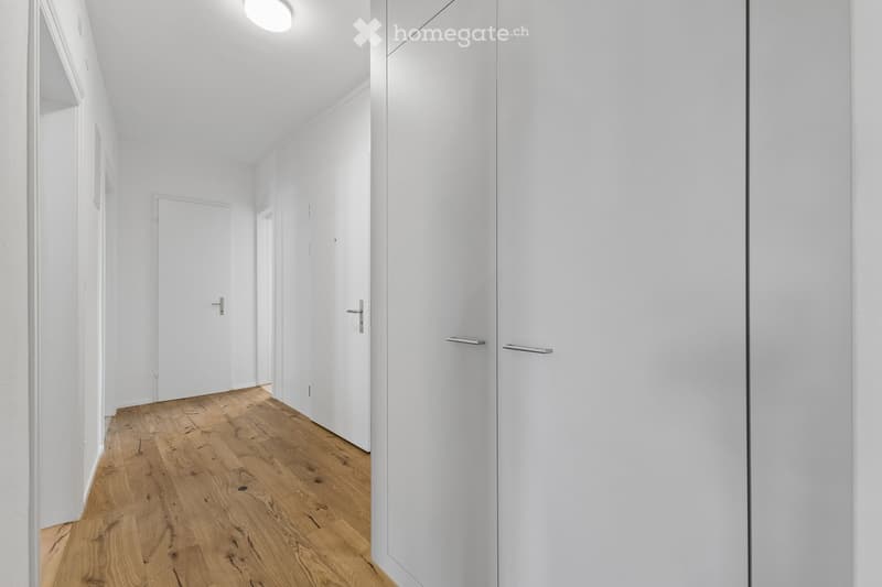 Modern, minimalist hallway with white walls, wooden flooring, and several closed white doors.