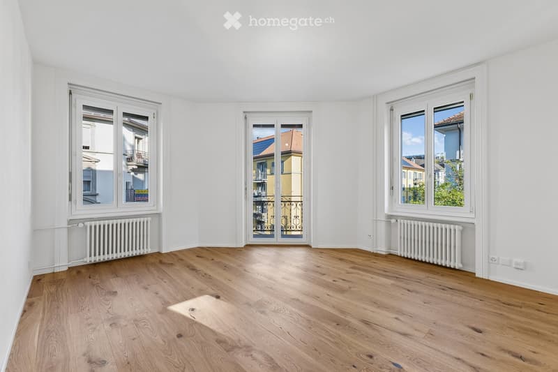Empty room with wooden flooring, white walls, large windows, and radiators. No furniture or equipment present.