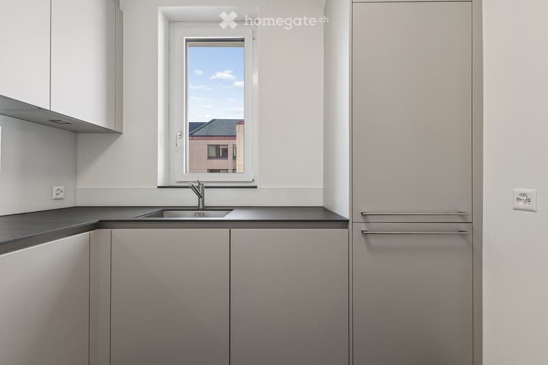 Modern kitchen with white cabinets, a stainless steel sink, and a window overlooking a building.