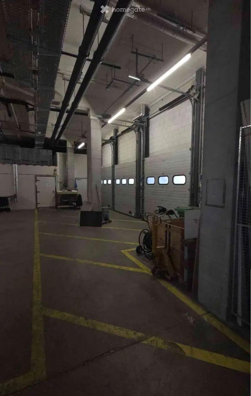 Empty industrial-style garage with concrete floors, exposed pipes, and large garage doors. No furniture or equipment visible.