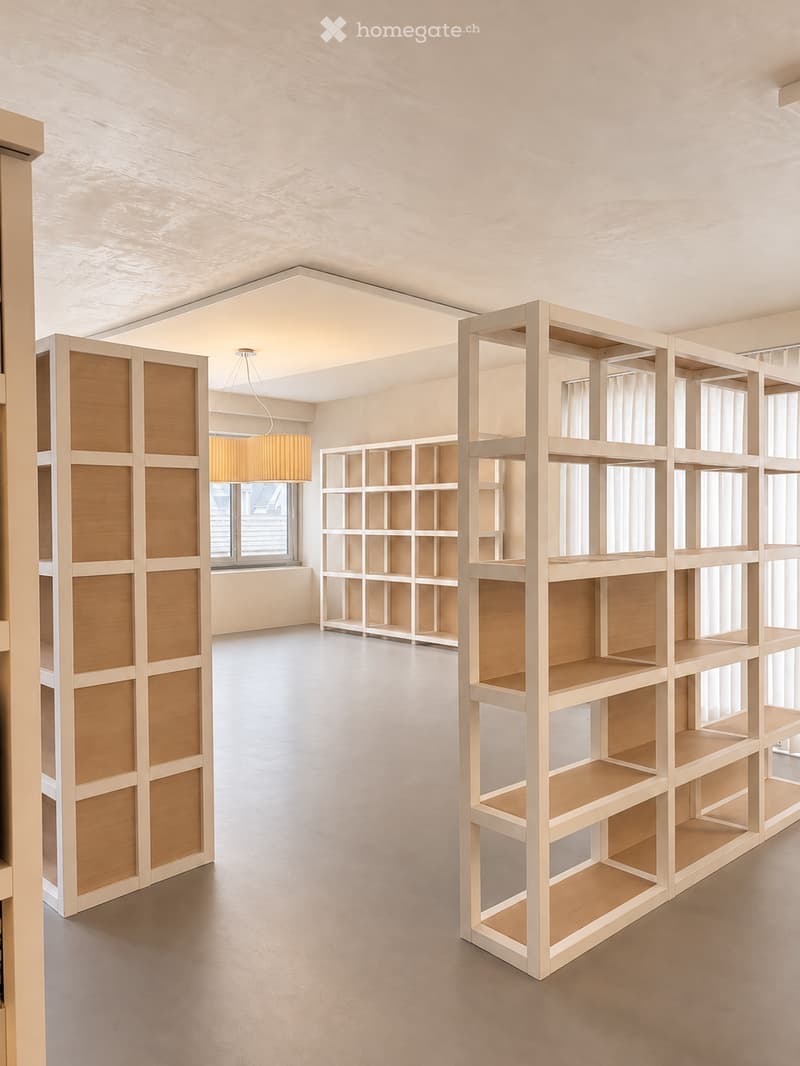 Empty room with wooden shelving units, large windows, and a hanging light fixture.