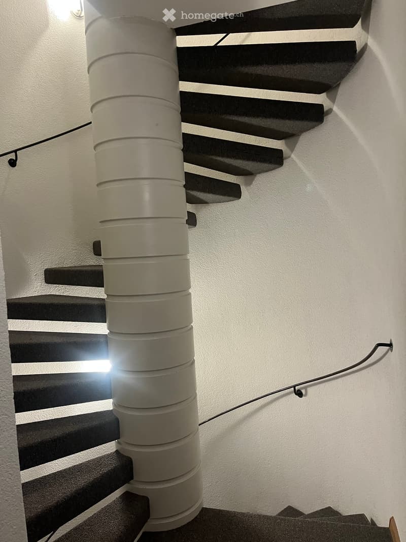 Modern staircase with black steps and a central cylindrical light fixture, white walls, and a sleek design.