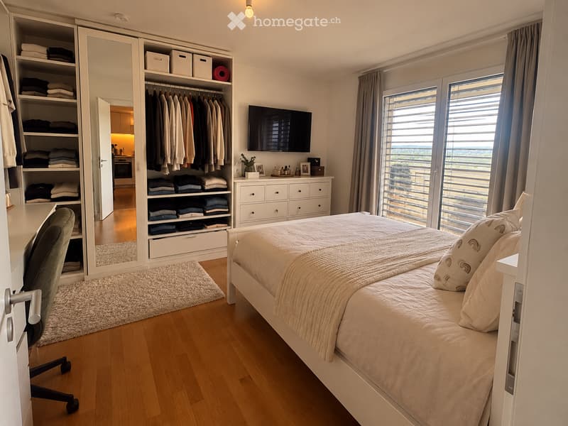 Modern bedroom with a large bed, a wardrobe, a dresser, a television, and a view through large windows.
