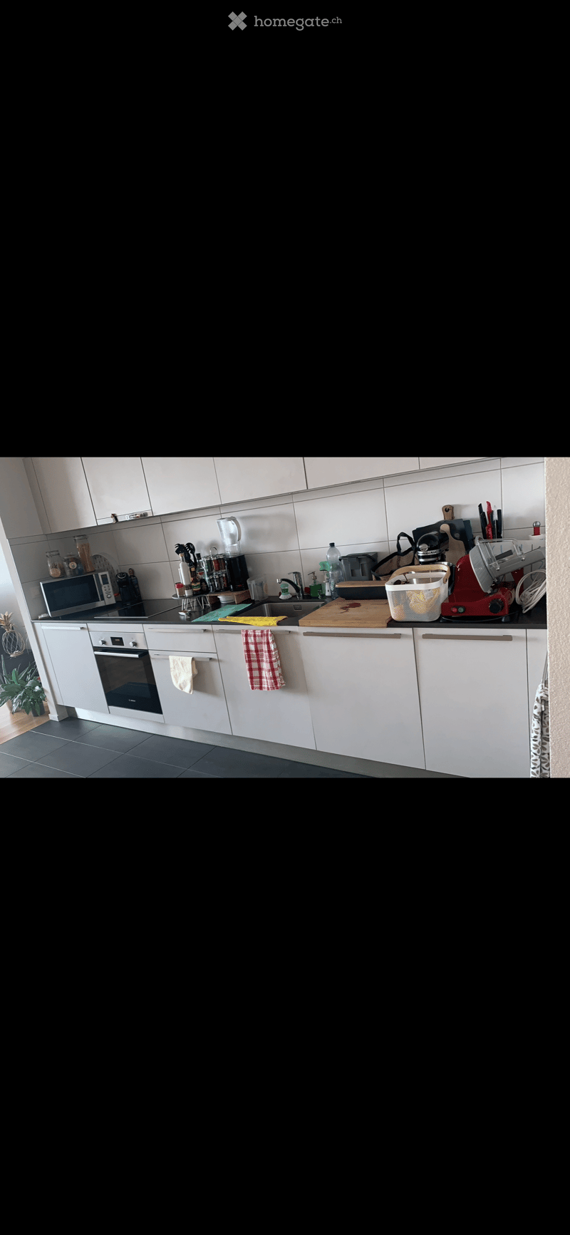 Modern kitchen with white cabinets, stainless steel appliances, and a black countertop. Visible items include an oven, microwave, sink, and various kitchen tools.
