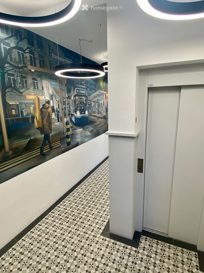 Modern hallway with patterned tile floor, white walls, and circular pendant lights. A large mural depicting a city street scene is visible on one wall.