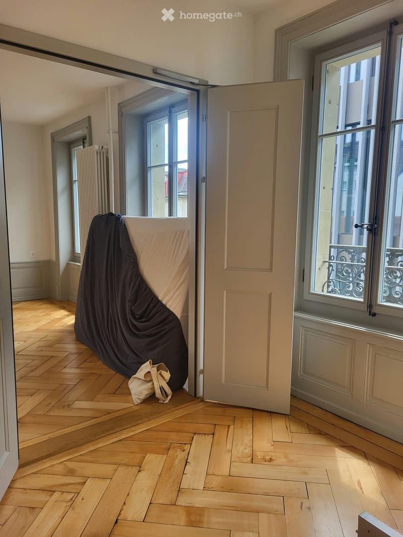 Empty room with wooden herringbone flooring, large windows, and a partially open door leading to a balcony area.