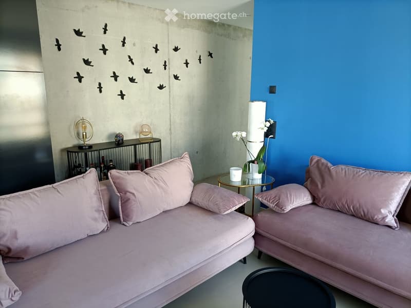 Modern living room with a pink sofa, coffee table, table lamp, decorative items, and a vase with flowers on a small round table.