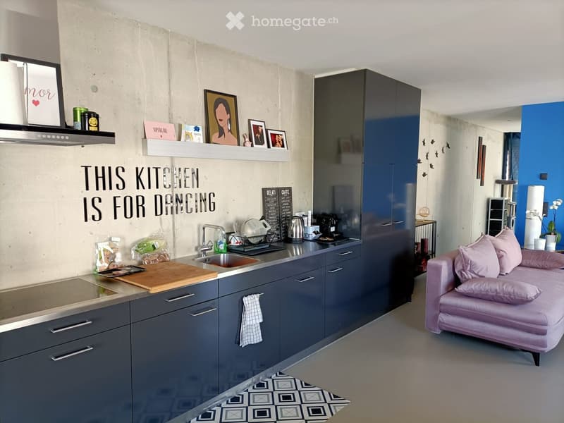 Modern kitchen with grey cabinets, stainless steel appliances, a wooden cutting board, and a pink sofa in the adjacent living area.