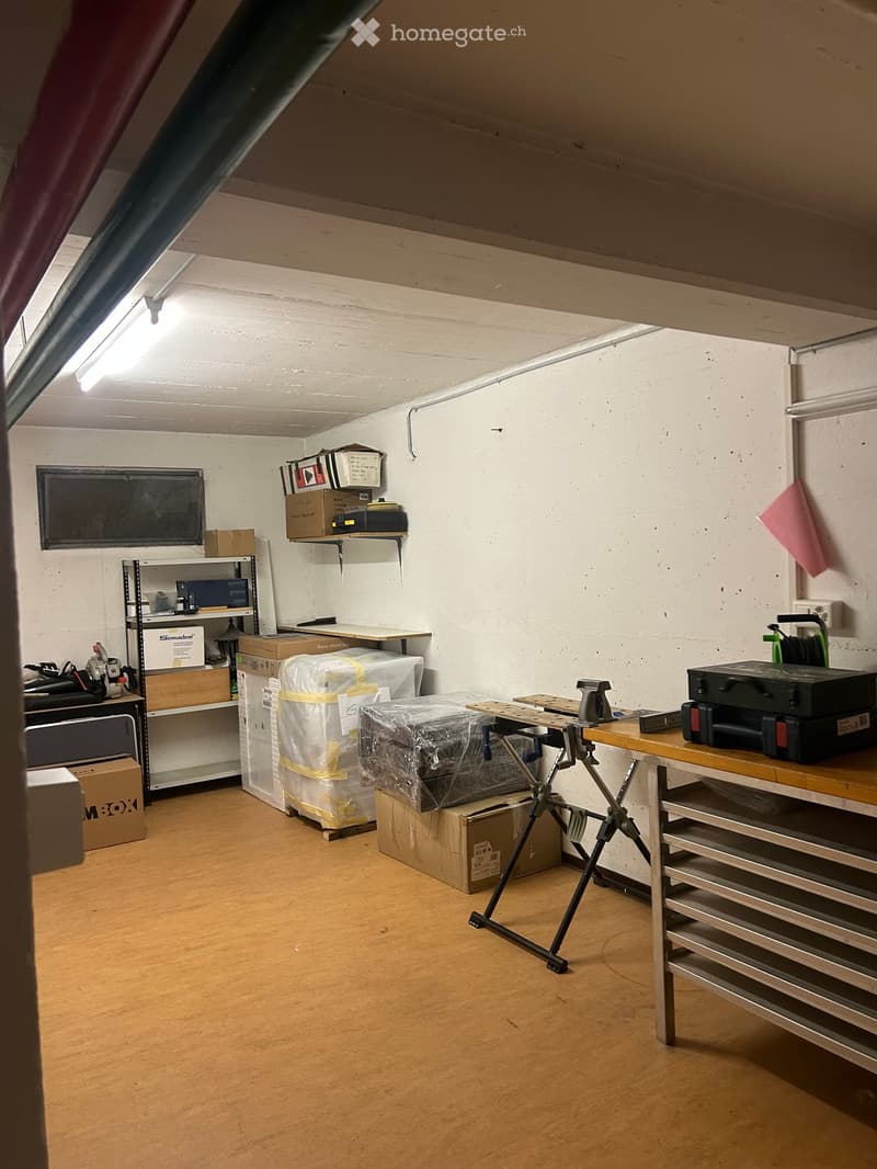 Workshop or storage room with wooden floor, shelves, and various tools and boxes.