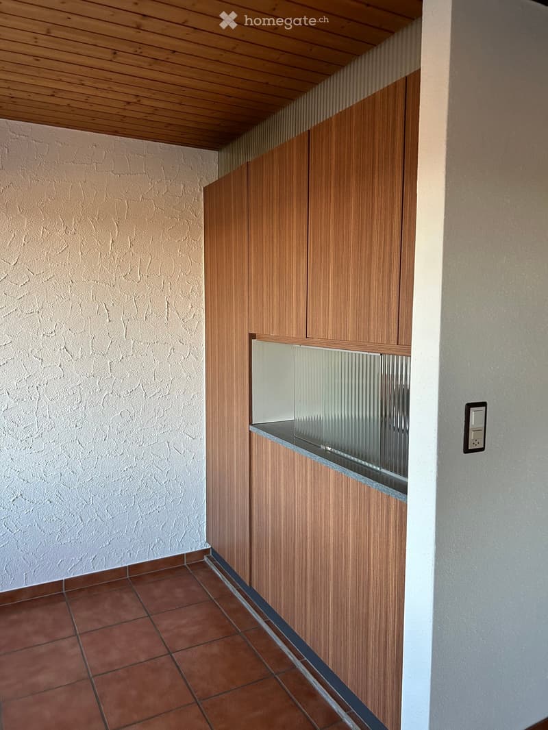 A narrow hallway with wooden paneling, tiled floor, and a small glass-enclosed shelf on the wall.