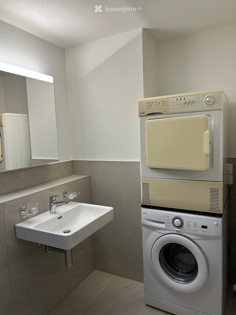 Bathroom with a white sink, mirror, and a stacked washer and dryer unit.