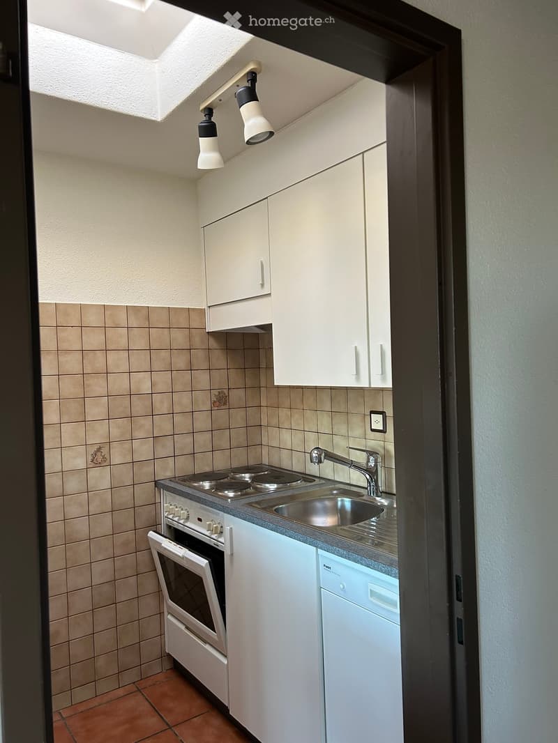 Compact kitchen with white cabinets, a four-burner electric stove, a sink with a faucet, and an oven. The walls are tiled in beige, and the floor is tiled in terracotta.