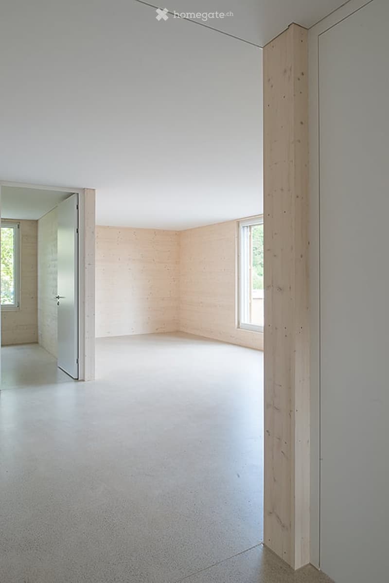 Completely empty room with light wooden walls, white ceiling, and concrete floor. No furniture or equipment.