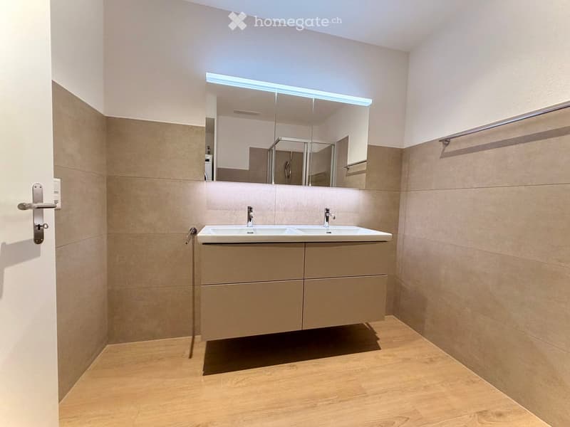Modern bathroom with a double sink, large mirror with LED lighting, and beige tiled walls.