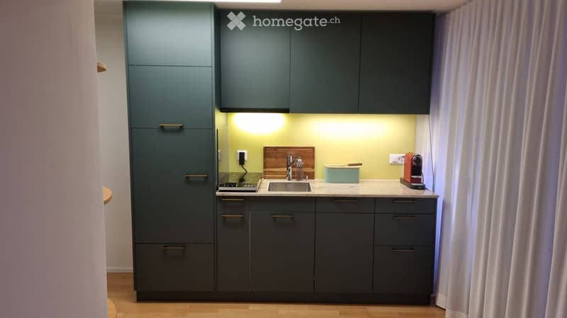 Modern kitchen with dark grey cabinets, a stainless steel sink, a small stove, and a coffee maker on the counter.