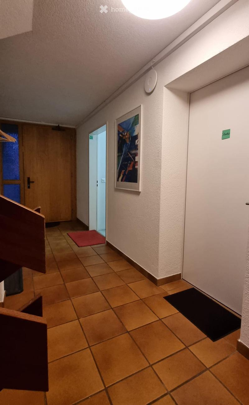 Hallway with tiled floor, white walls, a framed picture, and a small red mat near an open doorway.
