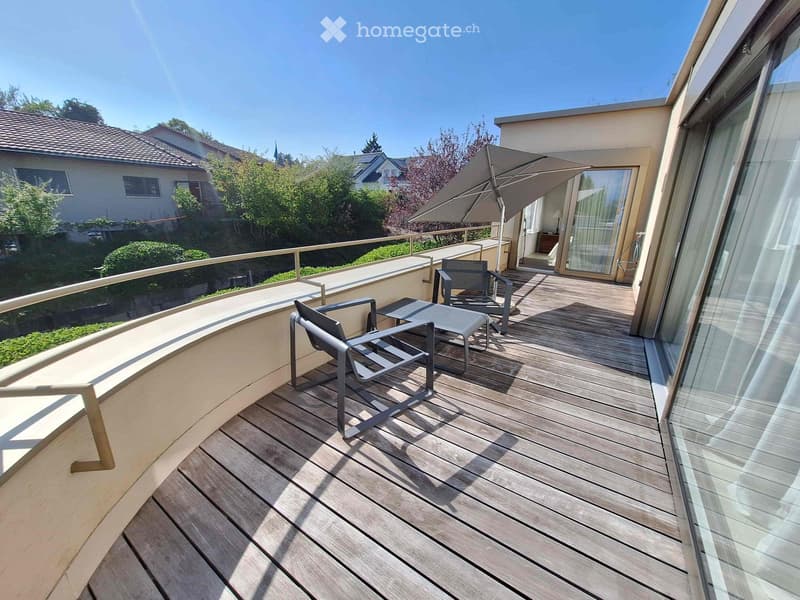 Wooden deck with two chairs, a small table, and an umbrella, overlooking a residential area with greenery.