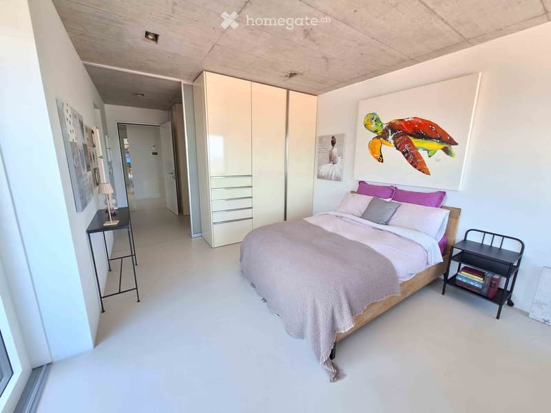 Modern bedroom with a large bed, nightstands, a lamp, and a large artwork on the wall. The room features white walls, a white floor, and built-in storage cabinets.