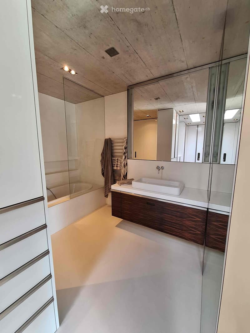 Modern bathroom with a white sink, dark wooden cabinet, large mirror, and a bathtub with a glass enclosure.