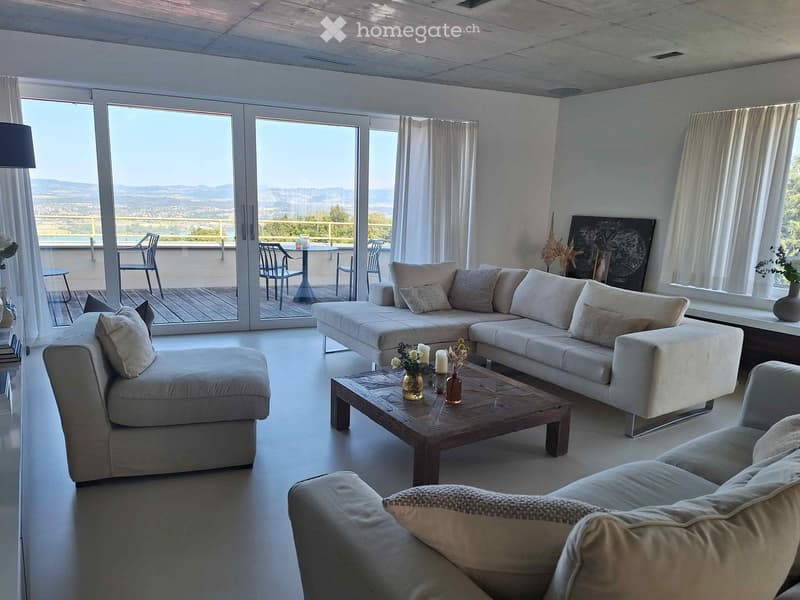Modern living room with large windows and a view, featuring a sectional sofa, coffee table, and outdoor seating area.