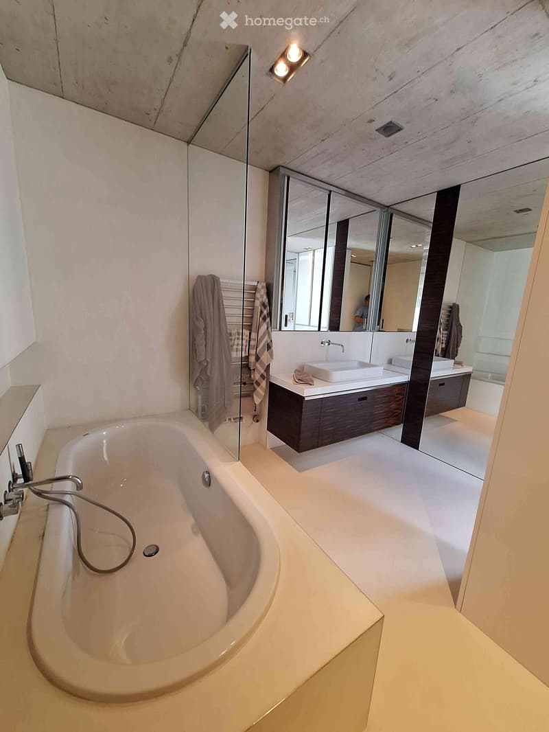 Modern bathroom with a large freestanding bathtub, double sink vanity with dark wood cabinets, large mirror, and towels hanging on a rack.