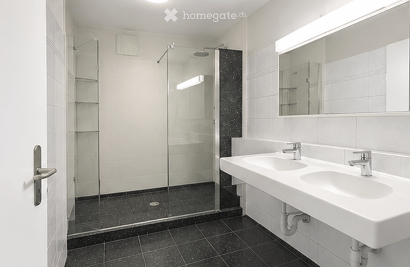 Modern bathroom with white tiles, black accents, double sink, large mirror, and glass-enclosed shower.