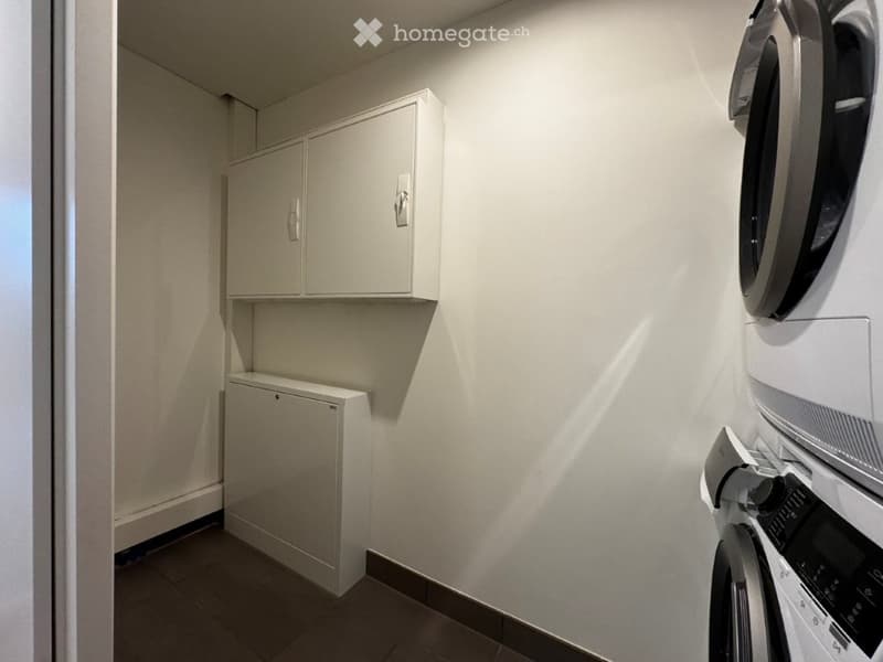 A small, well-lit room with a washing machine, dryer, and built-in cabinets.