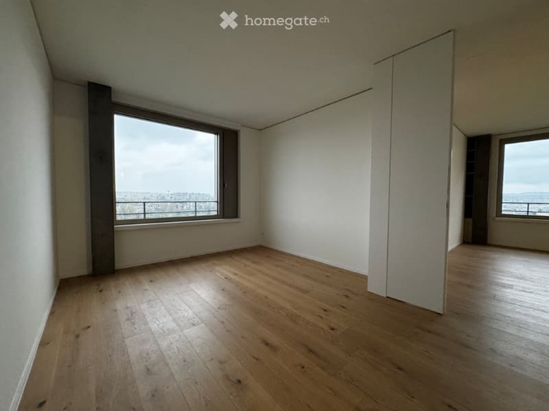 Empty room with wooden flooring, large windows offering a view, and white walls.